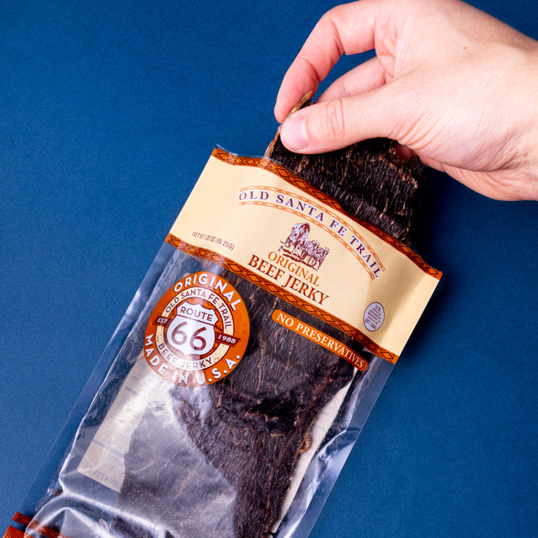 Hand holding a package of Old Santa Fe Trail beef jerky against a blue background