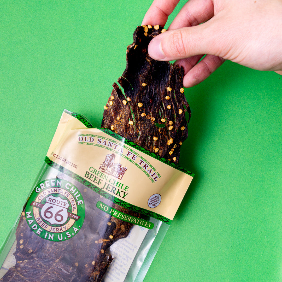 Hand picking up a package of Green Chile Beef Jerky from a green surface