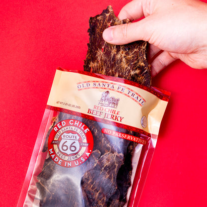 Hand holding a package of Old Santa Fe Trail Red Chile Beef Jerky against a red background