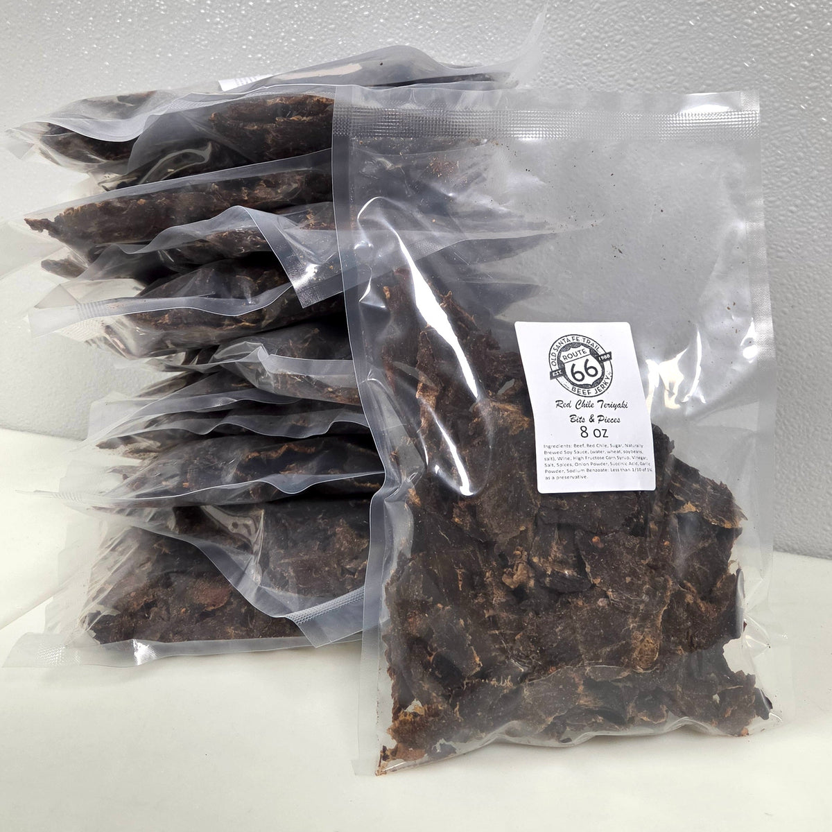 A stack of clear plastic bags filled with dark brown beef jerky, with one front bag showing a white label that reads 'Beef Jerky 8 oz'.